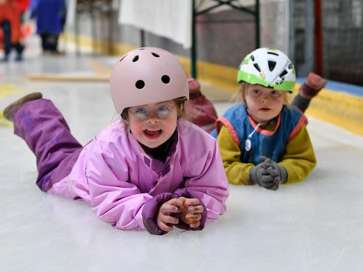 Zwei Kinder mit Helmen liegen lachend auf dem bemalten Eis