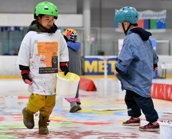 Kinder tragen Farbeimer über das bemalte Eis