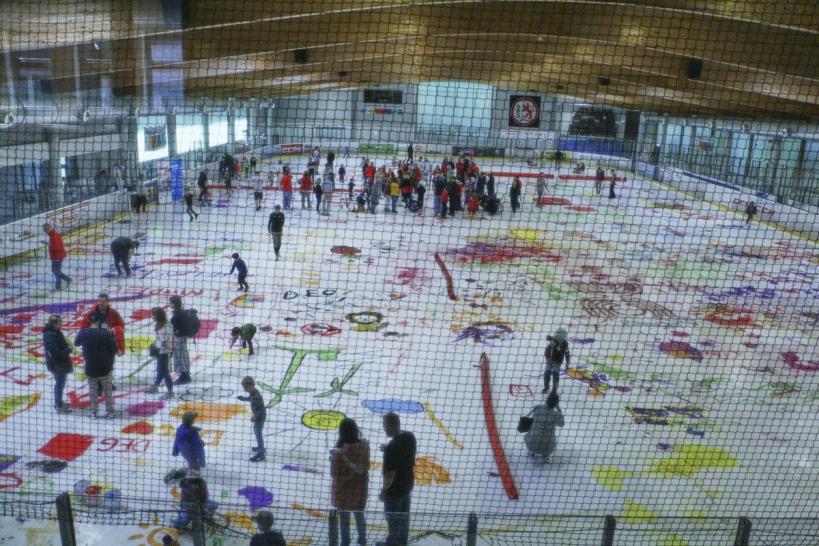 Vogelperspektive — Kinder und Künstler:innen bemalen die Eisfläche im Eisstadion Brehmstraße